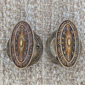 May include: Two antique oval-shaped door knobs with a decorative floral design in a brass finish.