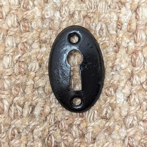 Op de afbeelding: Zwarte ovale sleutelgatbedekking met twee kleine gaten aan de zijkanten.