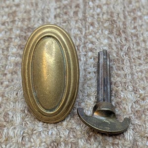 May include: A brass oval door knob with a decorative edge and a matching brass key with a T-shaped handle.