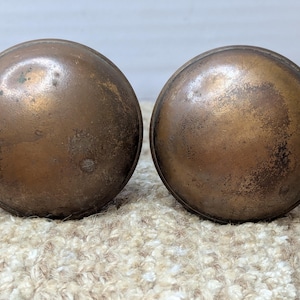 Peut inclure: Deux boutons de porte ronds en laiton avec une finition usée et vieillie.