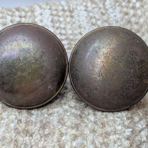 May include: Two antique brass door knobs with a worn, aged finish. The knobs are round and have a slightly raised edge.