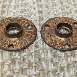 May include: Two antique brass door knobs with intricate floral designs and three holes each. The knobs are round and have a raised center with a hole in the middle.