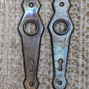 Peut inclure: Deux plaques de porte anciennes avec un trou de serrure et une ouverture circulaire. Les plaques sont en métal et ont une finition patinée et irisée.