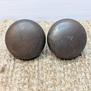 May include: Two dark brown round cabinet knobs with a slightly textured surface.
