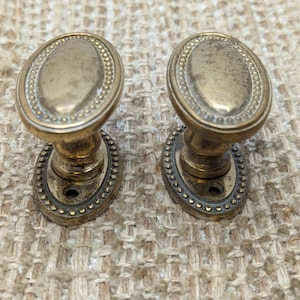 May include: Two antique brass door knobs with a beaded oval design. The knobs are in good condition with a slight patina.