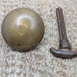 May include: A brass knob with a smooth, rounded surface and a dark brown metal hook with a threaded shaft.