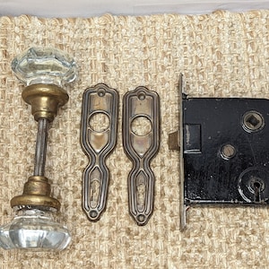 May include: Antique brass door hardware set with two clear glass knobs, two brass plates, and a black metal lock.
