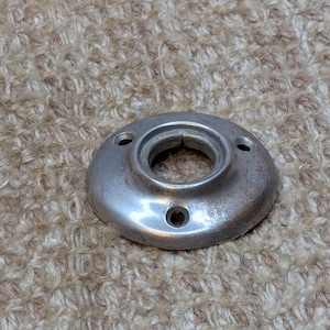 May include: A silver metal round plate with a hole in the centre and three small holes around the edge.