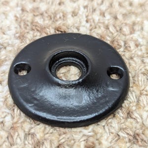 May include: Black metal round plate with a hole in the center and two smaller holes on the sides.