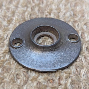 May include: A black metal round door plate with two small holes on the side and a larger hole in the center.