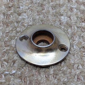 May include: A round, silver-toned metal plate with a hole in the centre. The plate has two small holes on the side.
