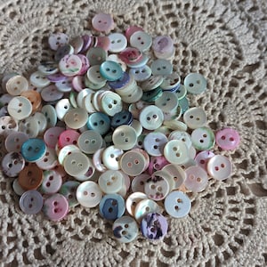May include: A collection of colorful, iridescent, two-hole buttons. The buttons are made of mother of pearl and have a variety of patterns and colors, including pink, blue, green, and white.