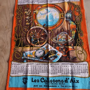 Puede incluir: Un paño de cocina vintage de 1986 con un tema náutico. El paño presenta un timón de barco, una escotilla, un globo terráqueo y un loro. El calendario está en francés e incluye los meses de enero a diciembre. El paño es naranja con acentos marrones y azules.