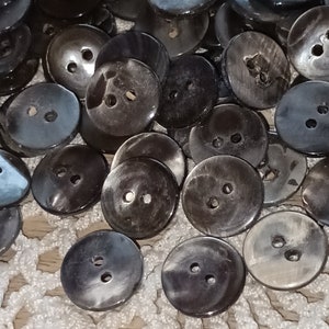 Peut inclure: Un ensemble de boutons en coquille noire et grise avec deux trous chacun. Les boutons sont disposés en pile et ont une finition lisse et polie.