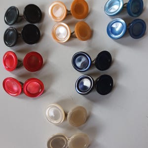 May include: Assortment of 10 pairs of decorative buttons in various colors, including black, red, blue, orange, and white. The buttons are round and have a smooth, shiny finish.