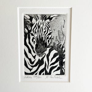May include: Black and white etching of a zebra's head and upper body, framed in a white mat. The zebra's stripes are detailed, and the artwork is signed and numbered "154/200" with the title "Zebra".