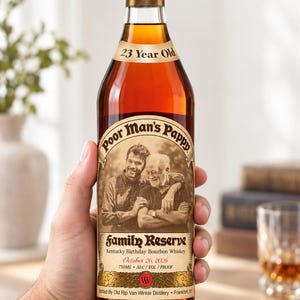 May include: A glass bottle of amber-coloured Kentucky Birthday Bourbon Whiskey labelled Poor Man's Pappy Family Reserve 23 Year Old. The label features a sepia-toned photograph of two men, the date October 26, 2026, and a volume of 750ml.
