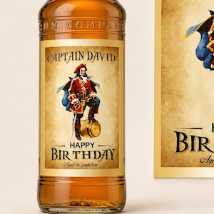 Może przedstawiać: Szklana butelka rumu Captain Morgan z personalizowaną etykietą przedstawiającą ilustrację pirata, tekst CAPTAIN DAVID, HAPPY BIRTHDAY oraz Aged to perfection. Obok znajduje się pasująca prostokątna naklejka z tą samą grafiką pirata i tekstem.