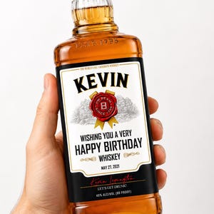 May include: A glass bottle of amber-coloured whiskey with a custom black and white label. The label features the name KEVIN, a red wax seal graphic, and the text WISHING YOU A VERY HAPPY BIRTHDAY, MAY 27, 2021, and 40% ALC/VOL (80 PROOF).