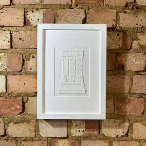 May include: A white framed print of a paper cut-out design of a building with intricate details. The design is in a white color and is framed in a white frame.