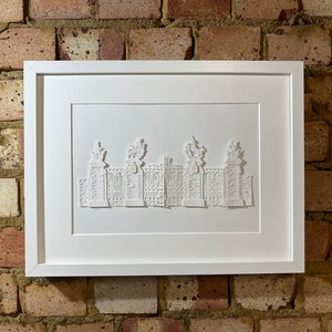 May include: A white framed paper art piece depicting a detailed, three-dimensional, paper-cut design of a gate with ornate details.