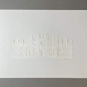 May include: A white paper cut-out of a large building with a central archway and multiple windows. The building is reminiscent of a castle or manor house. The artwork is signed "G.L. Owen" in the bottom right corner.