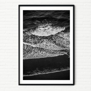 May include: Black and white photograph of ocean waves crashing on a beach. The waves are breaking into white foam and the water is dark.