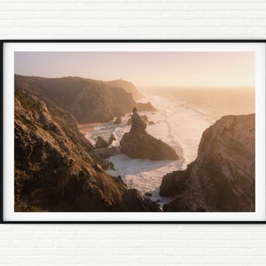 May include: A panoramic view of a rugged coastline with dramatic cliffs and rocky inlets. The ocean is a vibrant blue, with white waves crashing against the shore. The sky is a soft orange, suggesting a sunset or sunrise.
