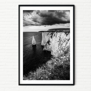 Può includere: Una fotografia in bianco e nero di una scogliera drammatica con una formazione rocciosa alta e appuntita nell'oceano. Il cielo è nuvoloso e l'acqua è mossa.