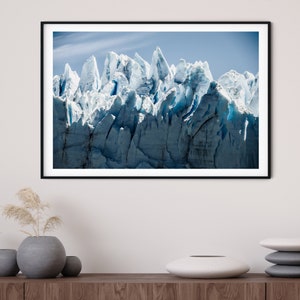 May include: A framed photograph of a glacier with a blue and white color scheme. The glacier is a large mass of ice and snow that has been sculpted by the wind and weather. The photograph is taken from a low angle, giving the viewer a sense of the glacier's vastness.