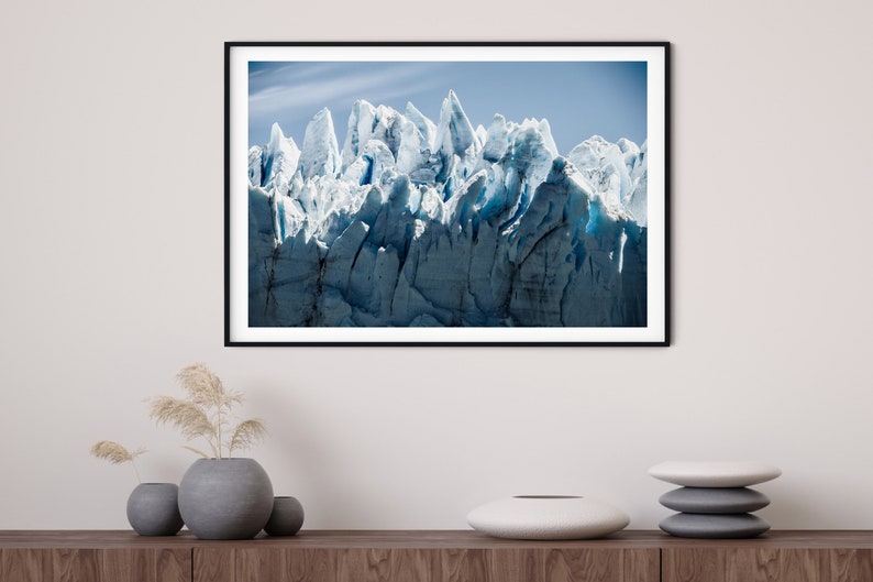 May include: A framed photograph of a glacier with a blue and white color scheme. The glacier is a large mass of ice and snow that has been sculpted by the wind and weather. The photograph is taken from a low angle, giving the viewer a sense of the glacier's vastness.