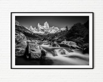 May include: Black and white framed landscape photograph of a mountain range with snow-capped peaks. A river flows through the foreground, with blurred water creating a sense of movement. The image is set against a clear sky.