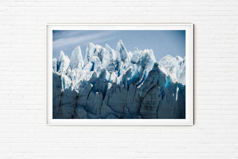 May include: A close-up view of a glacier with sharp, jagged edges. The ice is a bright blue and white color, and the sky is a clear blue.