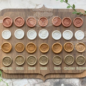 May include: A wooden board with 4 rows of 8 wax seals. Each row is a different color: rose gold, pearl, caramel, and gold. Each row has 8 different designs: clover, spike, ring, rose, bird, crown, flower, and a blank seal.