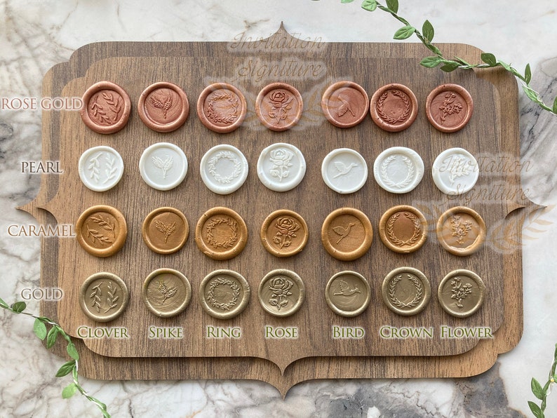 May include: A wooden board with 4 rows of 8 wax seals. Each row is a different color: rose gold, pearl, caramel, and gold. Each row has 8 different designs: clover, spike, ring, rose, bird, crown, flower, and a blank seal.