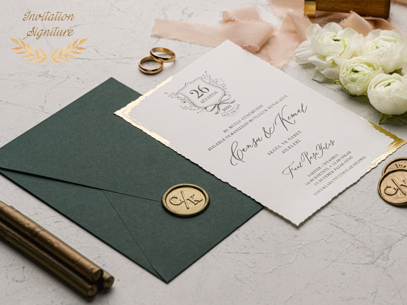 May include: A white wedding invitation with gold accents and a decorative border. The invitation features the text "Cansu & Kemal" and the date "26 August 2023".