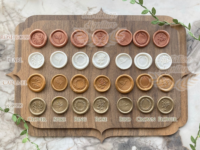 May include: A wooden board with 4 rows of 8 wax seals, each with a different design. The wax seals are in 4 colors: rose gold, pearl, caramel, and gold. The designs include a clover, spike, ring, rose, bird, crown, and flower.