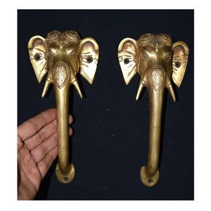 Könnte beinhalten: Zwei goldfarbene Messing-Türgriffe in Form von Elefantenköpfen mit aufwendigen Details. Die Griffe sind etwa 20 cm lang und haben ein traditionelles indisches Design.