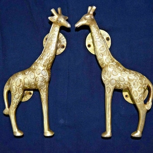 May include: A pair of gold-toned giraffe door handles with a textured finish. The handles are in a standing position with their heads turned towards each other.