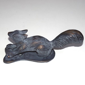 Op de afbeelding: Een bronzen eekhoornbeeldje in een rennende pose. De sculptuur heeft een gedetailleerde vachttextuur en is gemonteerd op een afgeronde basis. De staart van de eekhoorn krult omhoog. Geschikt voor woondecoratie.