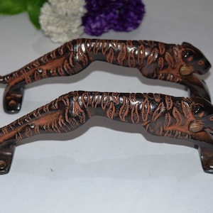 May include: Two black and brown tiger door handles with gold accents. The handles are made of metal and feature a detailed tiger design.