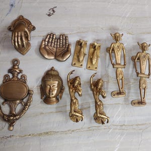 Peut inclure: Une collection de quincaillerie en laiton comprenant un heurtoir en forme de main, une paire de mains jointes, deux plaques en forme de poisson, un grand heurtoir orné, une tête de Bouddha, deux poignées dansantes et deux poignées à cornes.