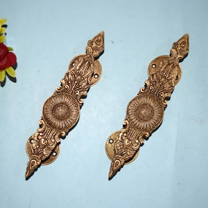 May include: Two ornate brass door handles with intricate floral designs. The handles are a light gold color and have a slightly aged finish.