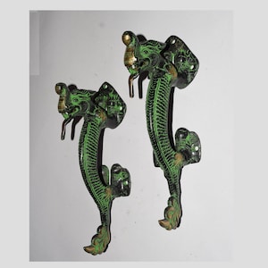 May include: A pair of green and gold metal door handles shaped like dragons. The handles feature intricate details and are a unique and decorative addition to any home.