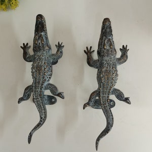 May include: Two antique-style alligator door handles with a distressed bronze finish. The handles are detailed with textured scales and have a realistic alligator design.