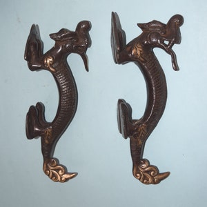 May include: A pair of antique bronze door handles shaped like dragons with gold accents. The handles are in the shape of a dragon with its head turned to the side and its tail curled around the handle.