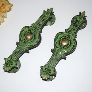 May include: A pair of ornate green and black door pulls with intricate floral designs. The pulls have a gold-colored accent in the center.