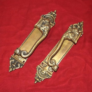 May include: Two ornate brass door handles featuring an elephant design. The handles are detailed with intricate carvings and have a gold finish.