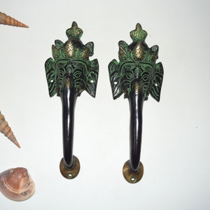 以下が含まれることがあります： 緑と金の仕上げが施された装飾的なドアノブのペア。ノブは、複雑なディテールが施された象の頭の形をしています。ノブは金属製で、黒色の仕上げが施されています。