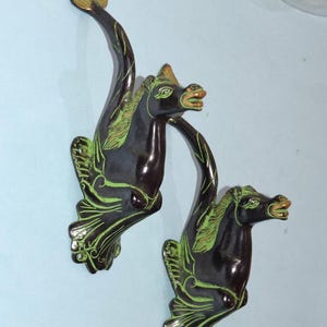 May include: Two decorative wall-mounted horse sculptures. The sculptures are dark brown with green accents, featuring a stylized horse head and flowing mane. The design includes a curved neck and a leaf-like tail.